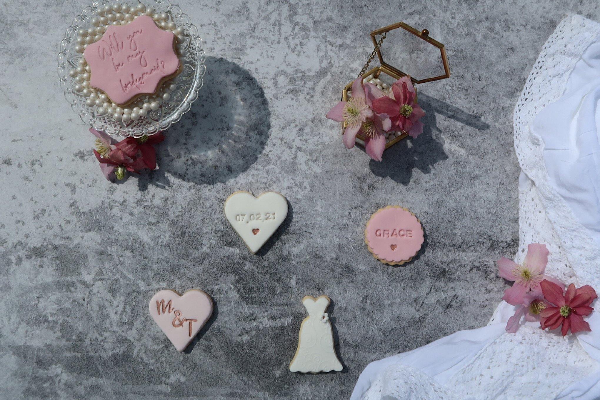 Will you be my bridesmaid proposal cookie set, pinks and rose gold, wedding dress cookie, heart cookie with wedding date, heart with bride and groom initials, round cookie with recipients name. Will you be my flower girl cookie and will you be my maid of honour cookie to side